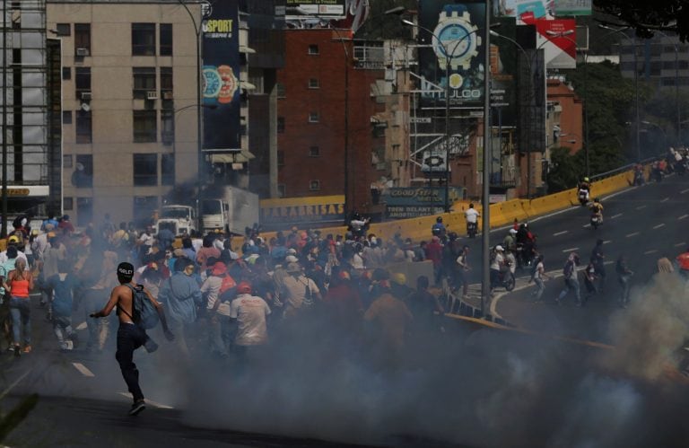 Demonstrators run away from tear gas fired by Bolivarian National Police officers during clashes between opposition members and police forces in Caracas, Venezuela, Tuesday, April 4, 2017. The demonstrators were trying to accompany opposition lawmakers in