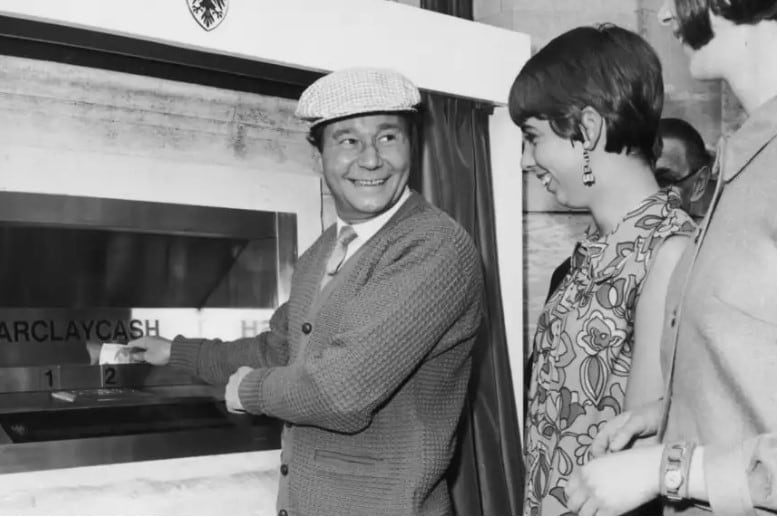 El actor cómico inglés Reg Varney retirando el primer billete de un cajero automático