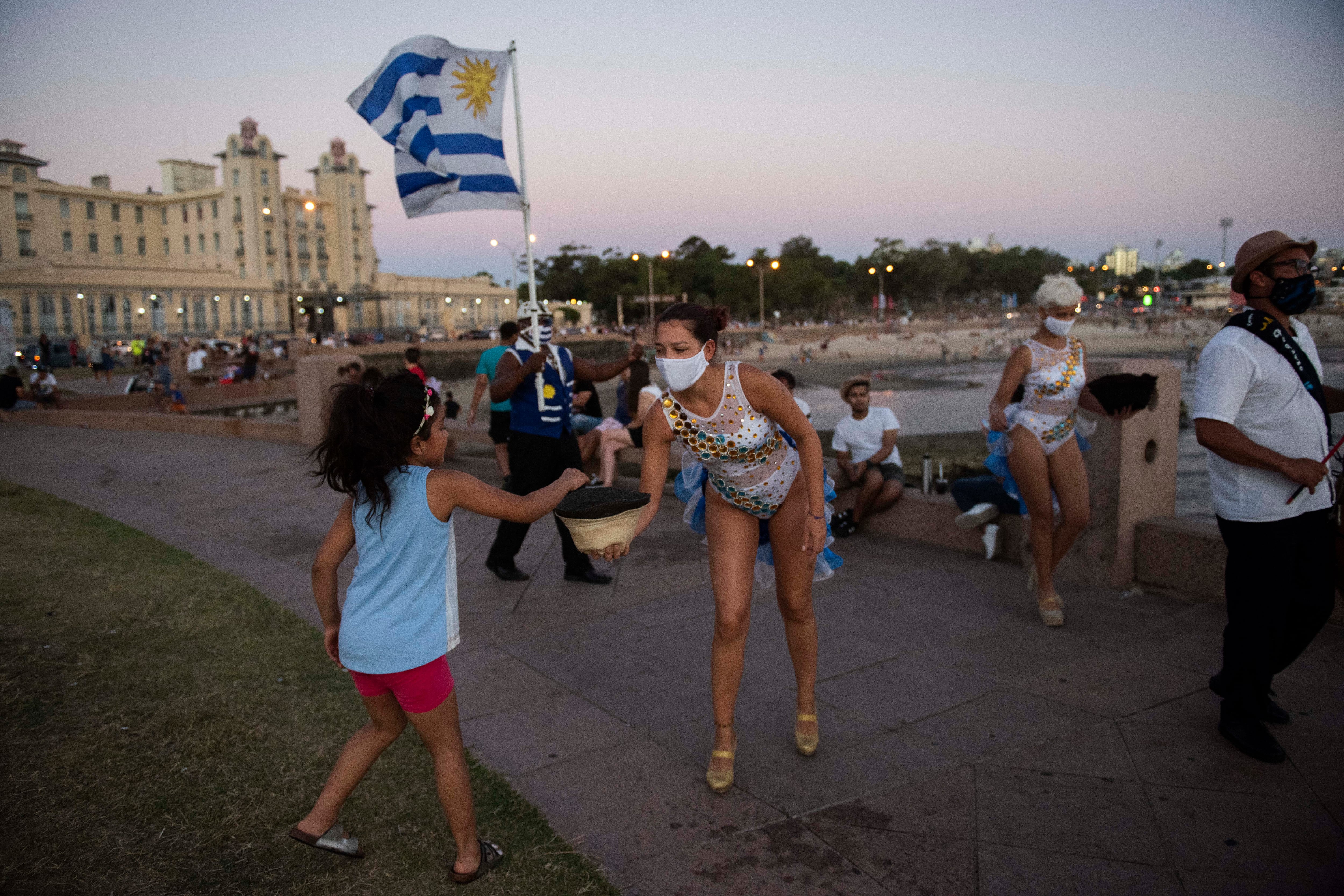 Una niña da una moneda a una artista de candombe que actúa en la Rambla de Montevideo, Uruguay