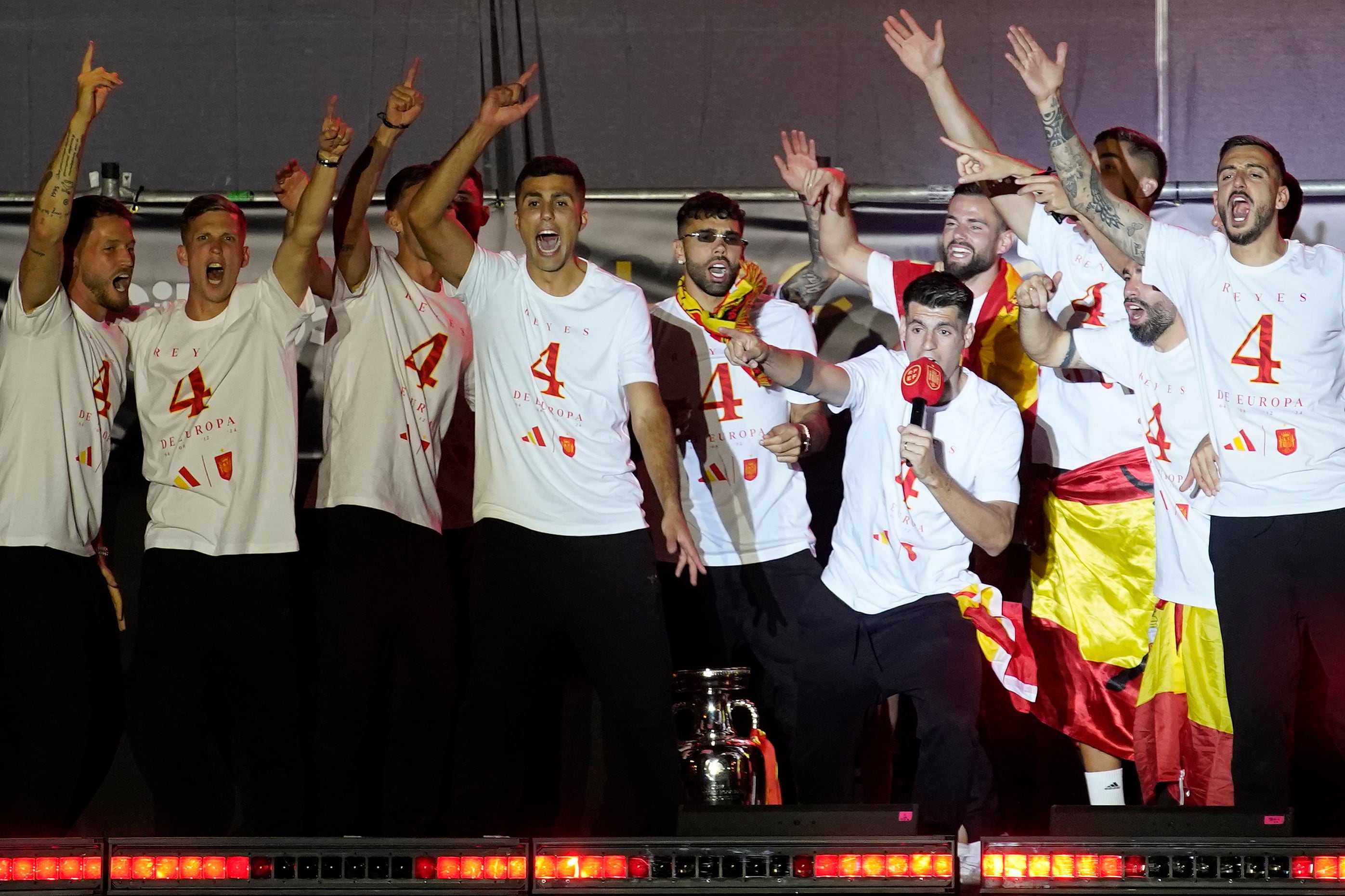 El capitán de la selección española, Álvaro Morata, con el micrófono, presenta al jugador Rodri, en el centro, a los aficionados durante las celebraciones del título de la selección española. (AP Foto/Andrea Comas)