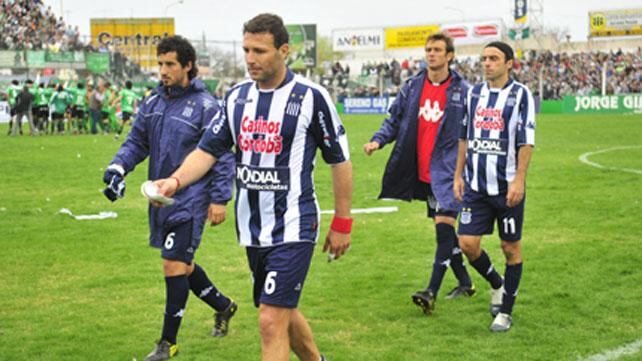 La alegría es de otros. El capitán de Talleres, Walter Ribonetto, se retira del campo de juego y atrás festejan jugadores e hinchas el triunfo de Sportivo Belgrano. // Foto: Sebastián Salguero