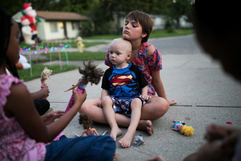 Bailey sostiene a Brody, su hermano menor, en la vereda de su casa. Crédito: Maddie McGarvey para The New York Times.