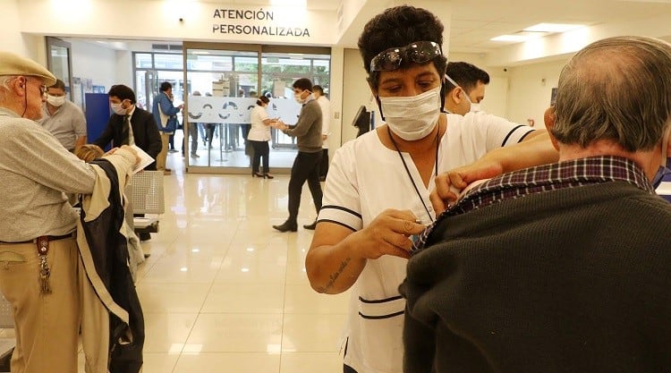 Jubilados reciben la vacuna contra la gripe y el neumococo, mientras se encuentran en los bancos cobrando sus haberes.