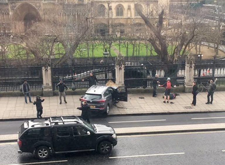 People stand near a crashed car and a injured person lying on the ground, right, on Bridge Street near the Houses of Parliament in London, Wednesday, March 22, 2017. Britain has been targeted Wednesday by what authorities are calling a terrorist incident,