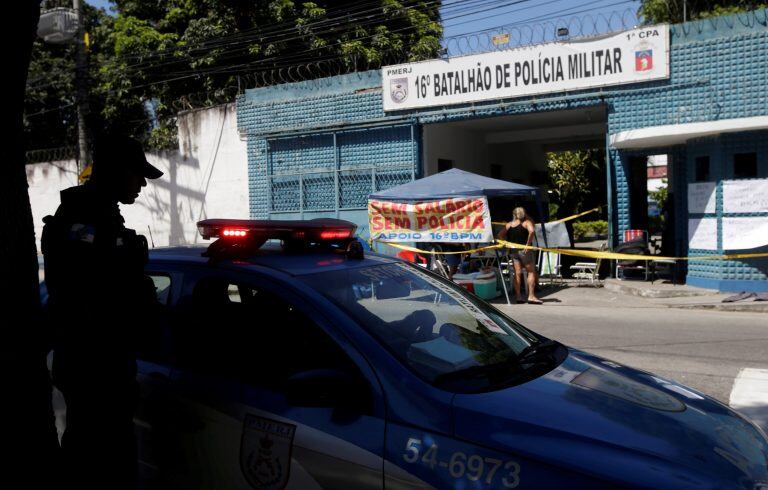 A policeman stands near a protest organised by family members of police officers in front of the entrance of a military police battalion in Rio de Janeiro, Brazil February 10, 2017. The banner reads: "Without salary, without police". REUTERS/Ricardo Morae