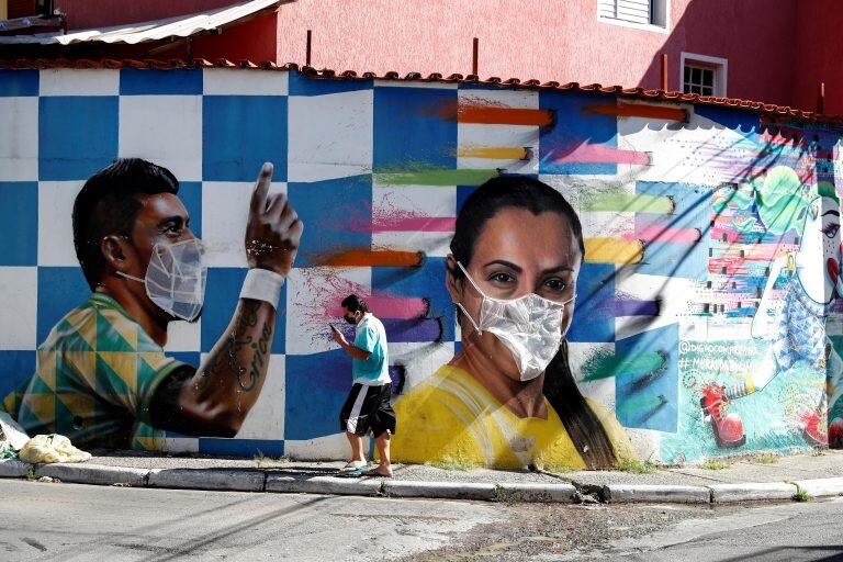 BRA50. SAO PAULO (BRASIL), 28/05/2020.- Un hombre camina frente a un grafiti con la imagen de los jugadores de fútbol de Brasil, Paulinho y Marta, realizado por el artista Rodrigo Rodrigues, conocido como Digãocomprimido, que pone máscaras en algunas de sus obras callejeras para crear conciencia sobre el coronavirus en Brasilandia, un barrio en la periferia de la ciudad con el mayor número de muertes por covid-19 hoy, jueves en Sao Paulo. EFE/Sebastião Moreira