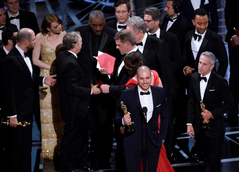 Fred Berger, producer of "La La Land," foreground center, gives his acceptance speech as members of PricewaterhouseCoopers, Brian Cullinan, holding red envelope, and Martha L. Ruiz, in red dress, and a stage manager discuss the best picture announcement e