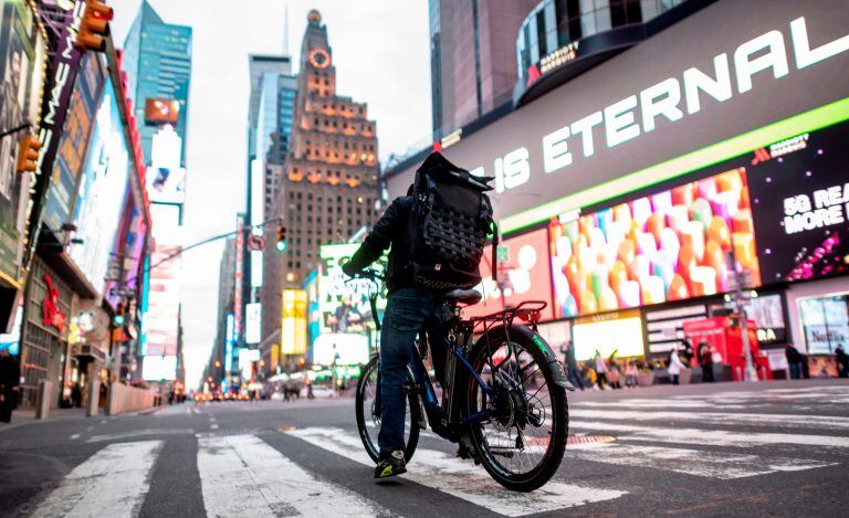 TOPSHOT - A food delivery man crosses the street in Times Square in Manhattan on March 17, 2020 in New York City. - Food delivery workers have become essential in New York after the city closed restaurants and bars to the public on March 16th, 2020. The coronavirus outbreak has transformed the US virtually overnight from a place of boundless consumerism to one suddenly constrained by nesting and social distancing. (Photo by Johannes EISELE / AFP)