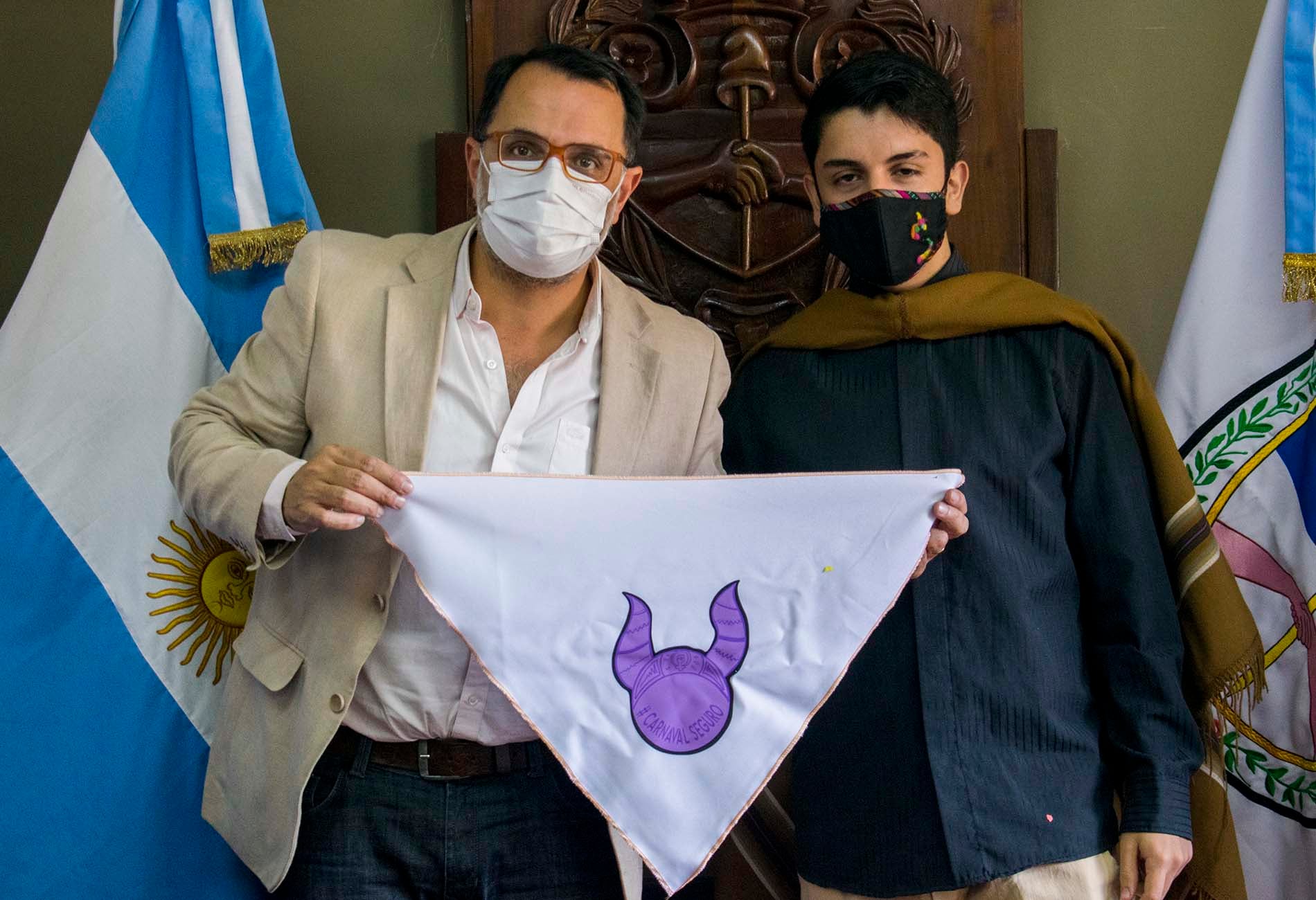 El concejal Aguiar y Lautaro Menacho sostienen un pañuelo con el símbolo de la campaña "Carnaval Seguro", que procura sumar elementos a la erradicación de la violencia de género.