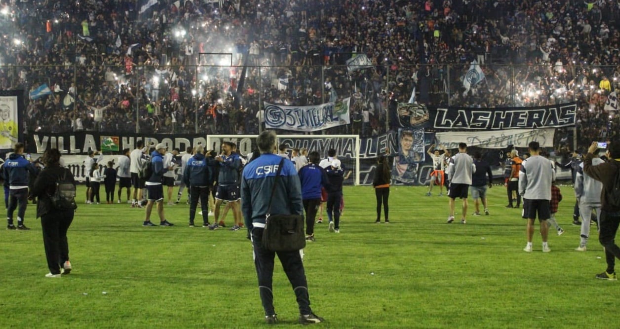 Gabriel Gómez, de espalda, con buzo y su maletín, disfruta uno de sus últimos momentos como técnico, junto a la popular de Independiente Rivadavia.