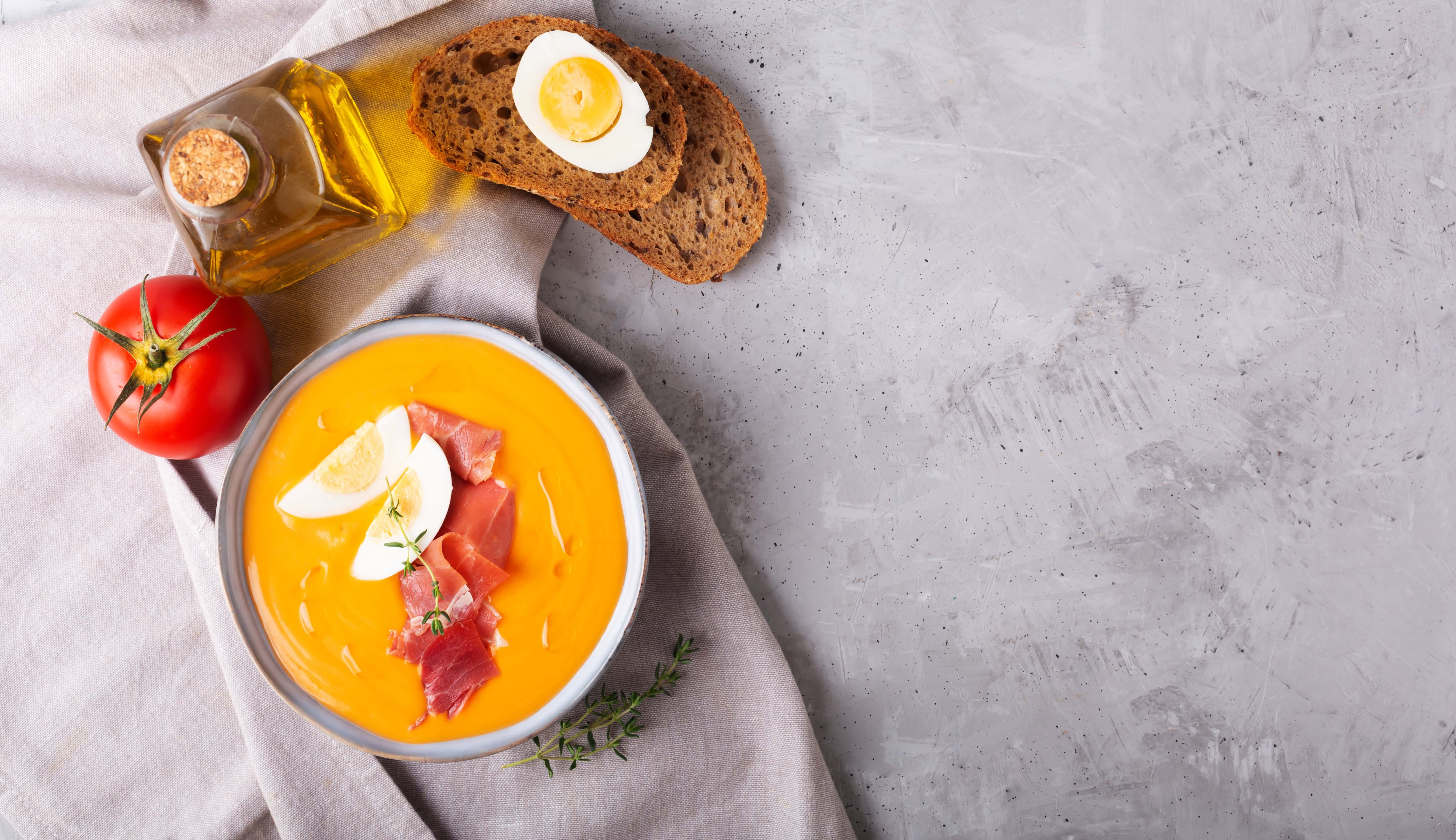 Salmorejo cordobes typical spanish tomato soup similar to the gazpacho, topped with jamon serrano and eggs on gray background, horizontal orientation