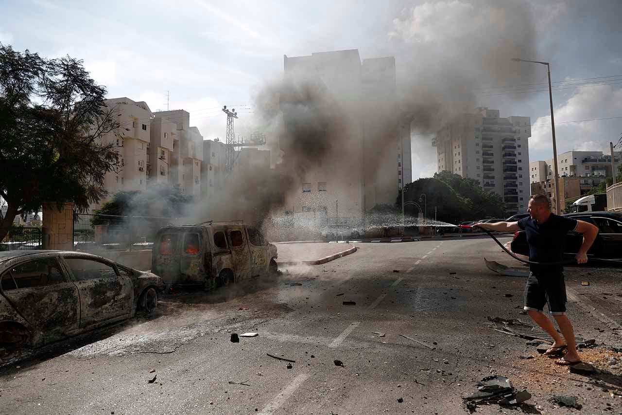 Ashkelon (Israel), 07/10/2023.- Un residente apaga vehículos en llamas en la ciudad israelí de Ashkelon tras el lanzamiento de cohetes desde Gaza, 07 de octubre de 2023. Se lanzaron andanadas de cohetes desde la Franja de Gaza a primera hora del sábado en un ataque sorpresa reivindicado por el Movimiento islamista Hamás. EFE/EPA/ATEF SAFADI