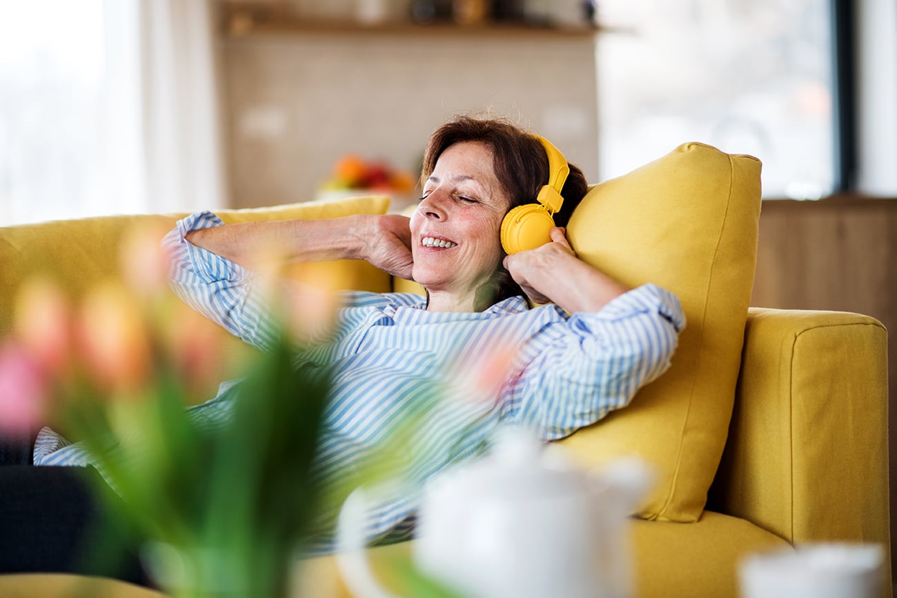 Mujer con auriculares en un sofá en casa, descansando.