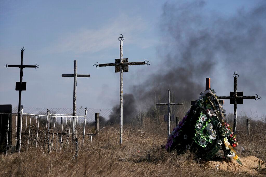 Las imágenes más impcatantes del conflicto. El humo de los proyectiles se eleva al fondo, una corona de flores honra a los caídos de la guerra en el cementerio de Vasylkiv, el suroeste de Kiev. Foto: AP / Vadim Ghirda