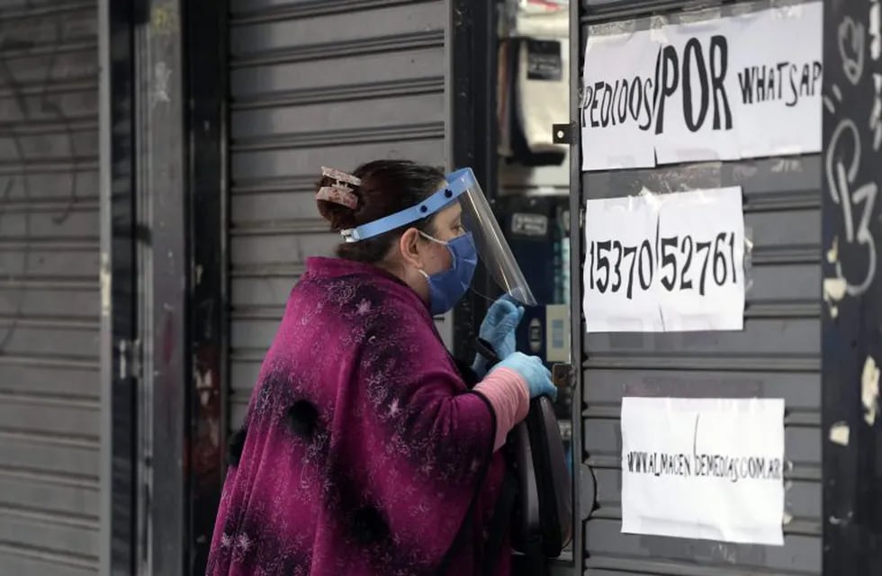 A woman wearing a face mask, shield and gloves takes away her order at a partially closed store during the lockdown imposed by the government against the spread of the new coronavirus- in Buenos Aires, Argentina, on May 22, 2020. - Argentina is expected to pass the 10,000 infections of COVID-19 since the first positive case on March 3. (Photo by JUAN MABROMATA / AFP)