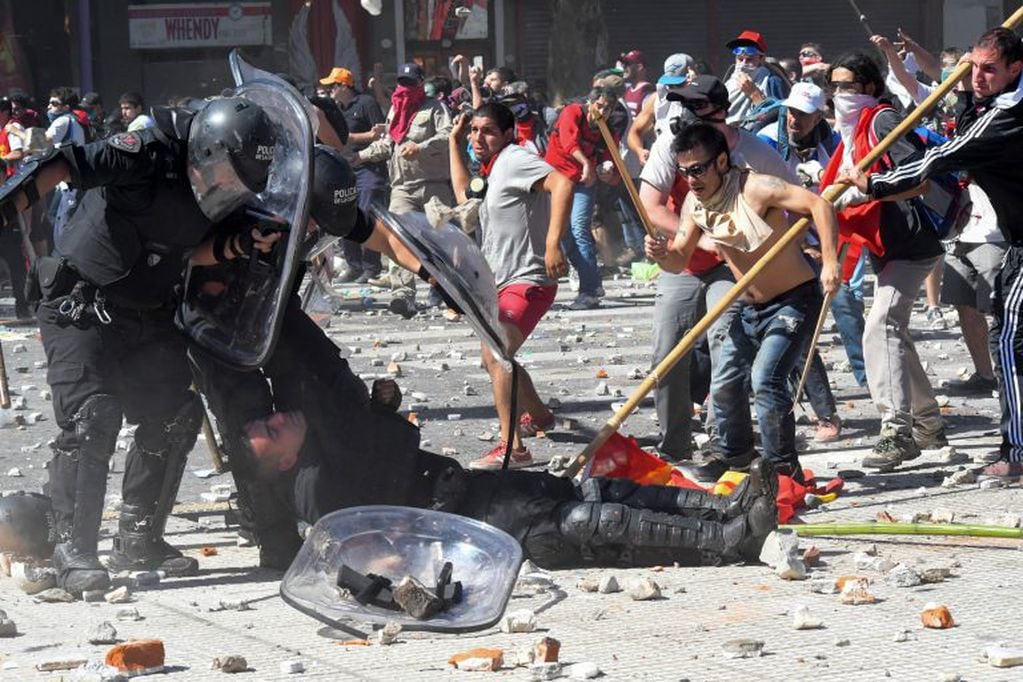 Dos policías miran atónitos hacia su compañero en el suelo mientras manifestantes les arrojan piedras durante la manifestación del 18/12/2017 en Buenos Aires, Argentina, contra la reforma del sistema de pensiones. (Foto: Laura Cano/telam)
