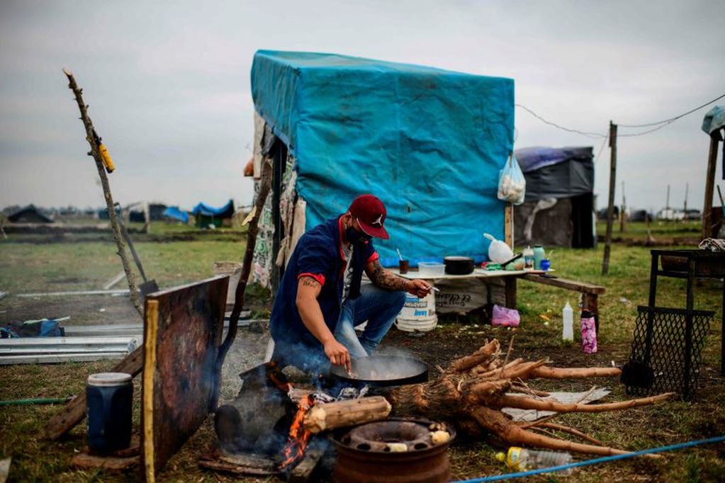 TOPSHOT - A man cooks outside a tent set up in land occupied by homeless people outside Guernica, in the province of Buenos Aires, south of the Argentine capital, on August 28, 2020 amid rising poverty in an economic crisis exacerbated by the COVID-19 novel coronavirus pandemic. - Outdoors or under makeshift tents, about 2,500 people have been defying justice, and COVID-19, for more than a month, when they occupied empty lots in Buenos Aires Province, the most populous of the country and where the pandemic is hitting the hardest. Scattered in over 100 hectares of vacant land, children run around and adults talk, while the police guards the area. Prevention measures against the novel coronavirus barely exist here. (Photo by Ronaldo SCHEMIDT / AFP)