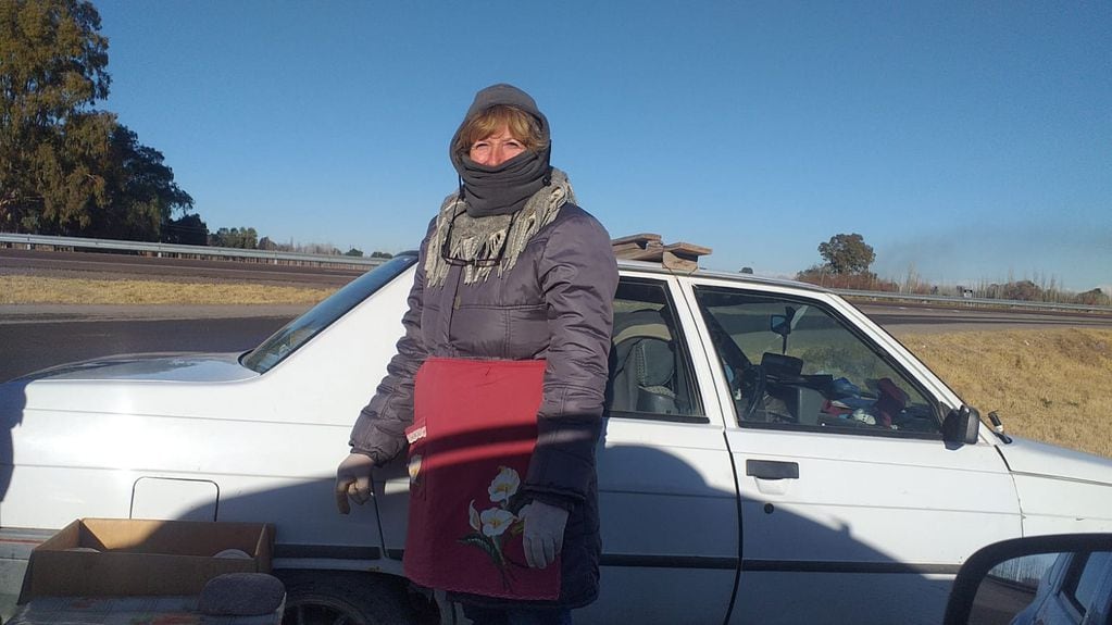La profesora de arte jubilada, junto al auto con el que llega hasta la ruta para vender café.