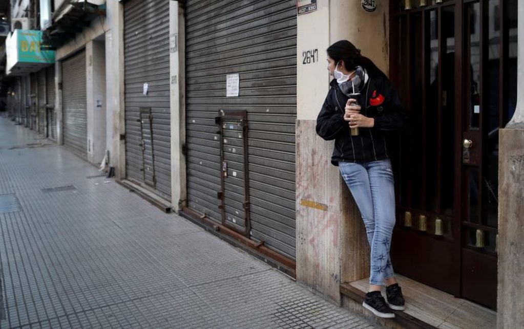 A woman drinking mate, looks down a street lined with shuttered businesses amid the new coronavirus pandemic, in Buenos Aires, Argentina, Friday, June 26, 2020. Argentine President Alberto Fernandez is expected to announce a rollback on restrictions of the COVID-19 lockdowns in place since March 20th. (AP Photo/Natacha Pisarenko)
